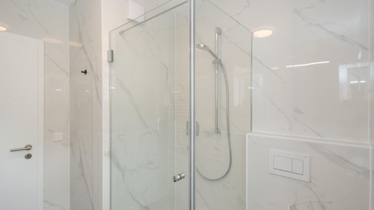 Een moderne douche met glazen deuren en een heldere, gemarmerde tegelontwerp. De ruimte oogt schoon en elegant.