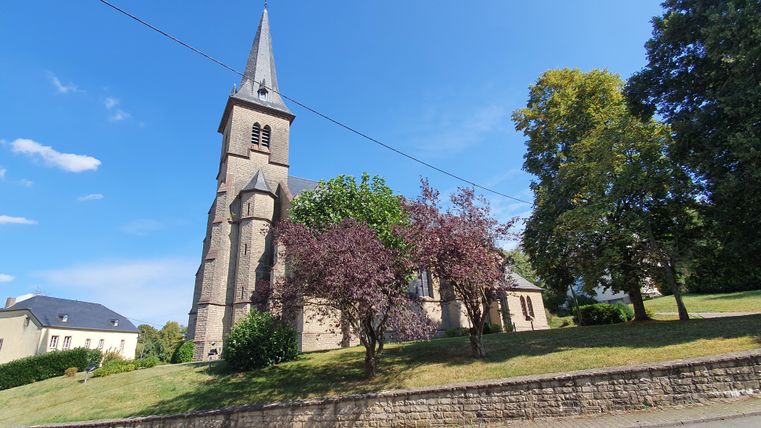 Pfarrkirche St. Bartholomäus mit spitzem Turm und Bäumen im Vordergrund.