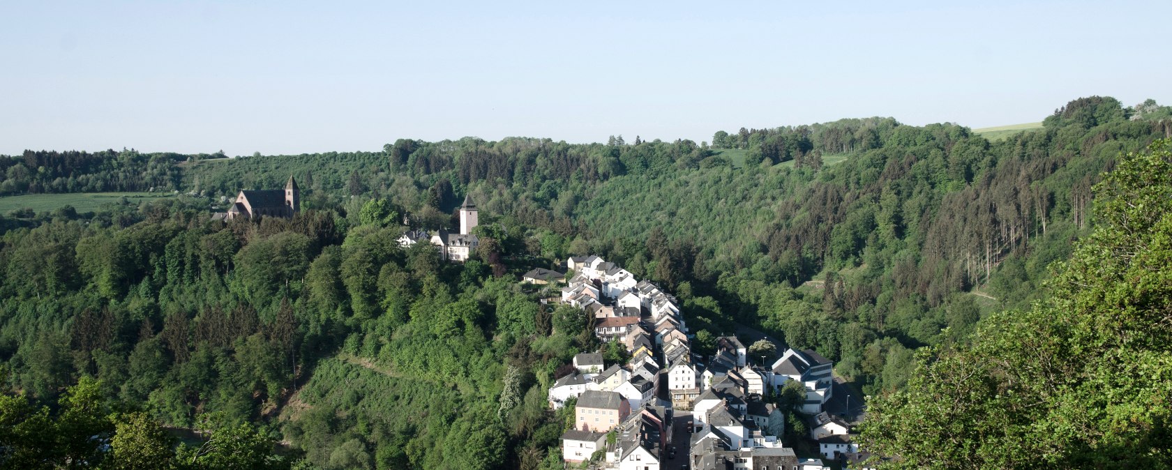 Panoramablick auf Kyllburg mit Kirche und Häusern, eingebettet in grüne Wälder unter klarem Himmel., © TI Bitburger Land