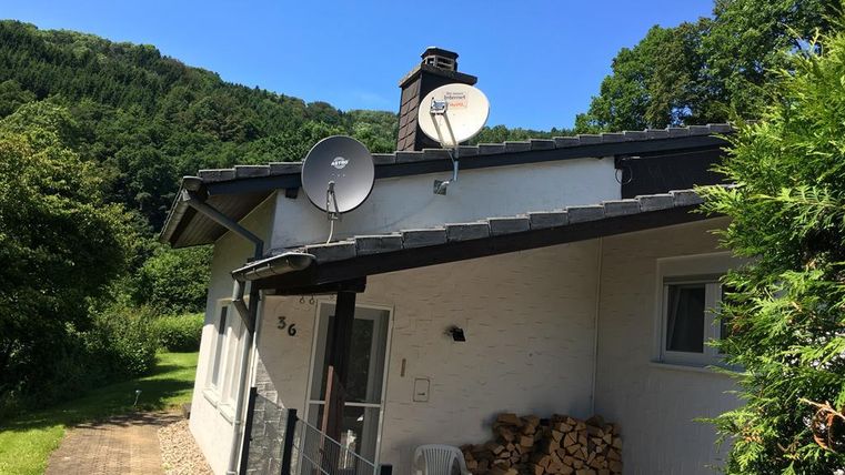 Ein gemütliches Haus mit Satellitenschüsseln und einem schönem Garten. Im Hintergrund sind grüne Hügel zu sehen.