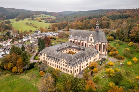 Blick auf eine Klosteranlage mit einer Kirche und einem Wohngebäude, umgeben von Wald