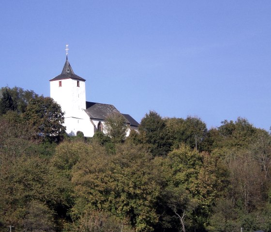 Die alte Kirche St Apollonia in Gransdorf thront auf einem bewaldeten Hügel unter klarem, blauem Himmel., © Doris Pauels
