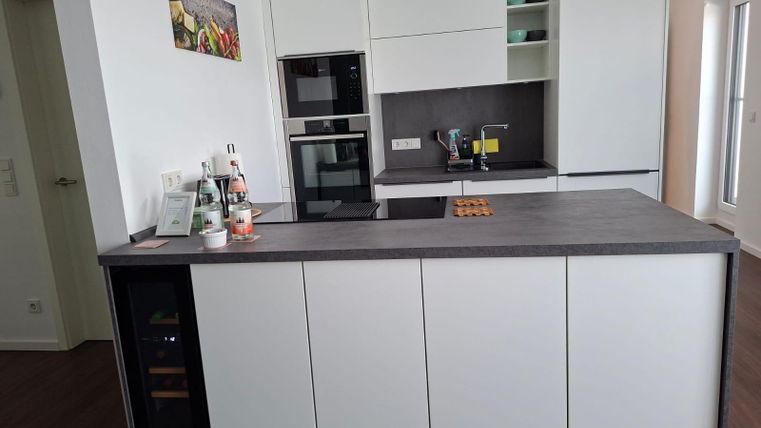 Une cuisine moderne avec des meubles blancs et un plan de travail en bois. Elle est bien équipée avec une cuisinière, un four et un évier.