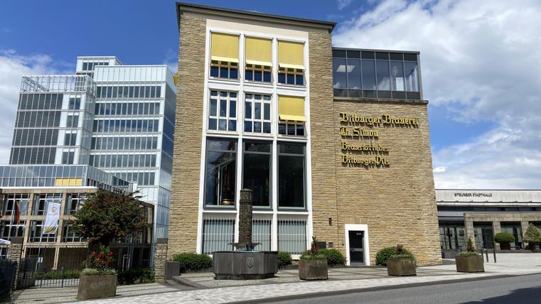 Een modern gebouw met grote ramen en gele jaloezieën. Op de achtergrond zijn nog meer moderne gebouwen te zien.