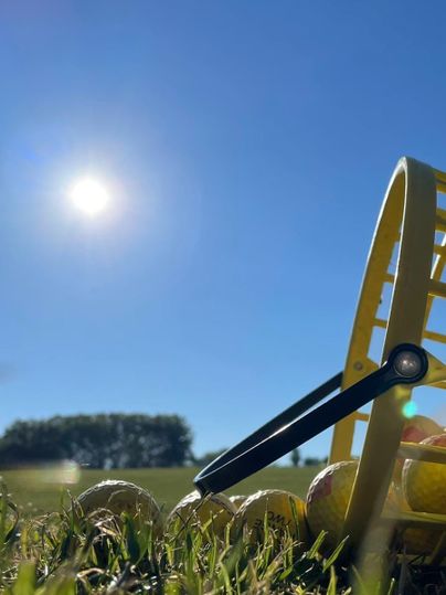 Eine Golfplatzszene mit einem Gelbkorb, gefüllt mit Golfbällen, liegt im Gras. Der klare blaue Himmel strahlt hell mit der Sonne.