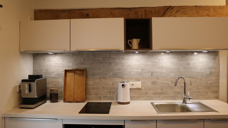 Een moderne keuken met lichte kasten en een elegante werkblad. De muren zijn gedecoreerd met grijze tegels en de verlichting zorgt voor een aangename sfeer.