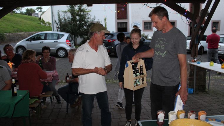 Eine Gruppenveranstaltung im Freien mit mehreren Personen. Zwei Männer und ein Mädchen stehen im Mittelpunkt und halten eine Geschenkbox.