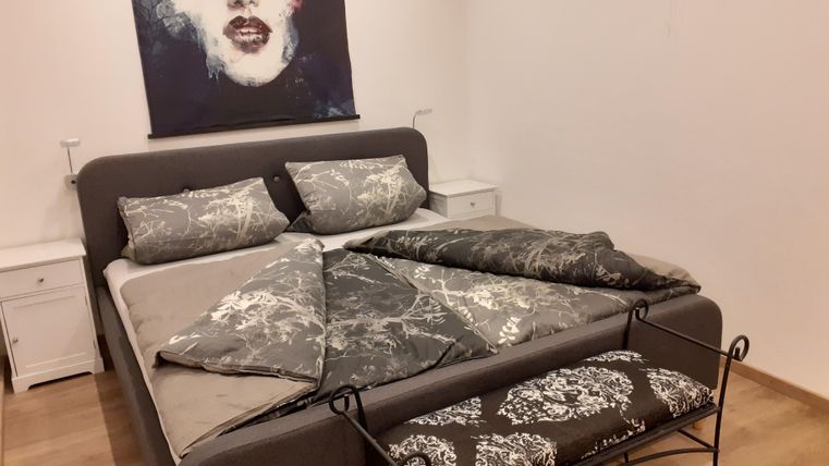 Een moderne slaapkamer met een groot bed en stijlvolle grijze beddengoed. Aan de muur hangt een kunstzinnig schilderij met een gezicht.