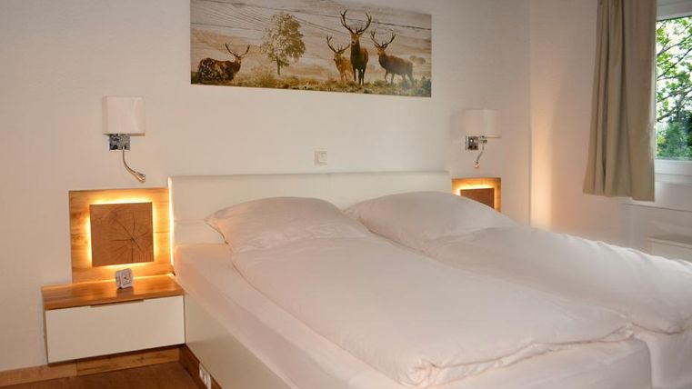 Ein gemütliches Schlafzimmer mit einem Doppelbett und sanfter Beleuchtung. An der Wand hängt ein Bild von Rehen in einer natürlichen Landschaft.