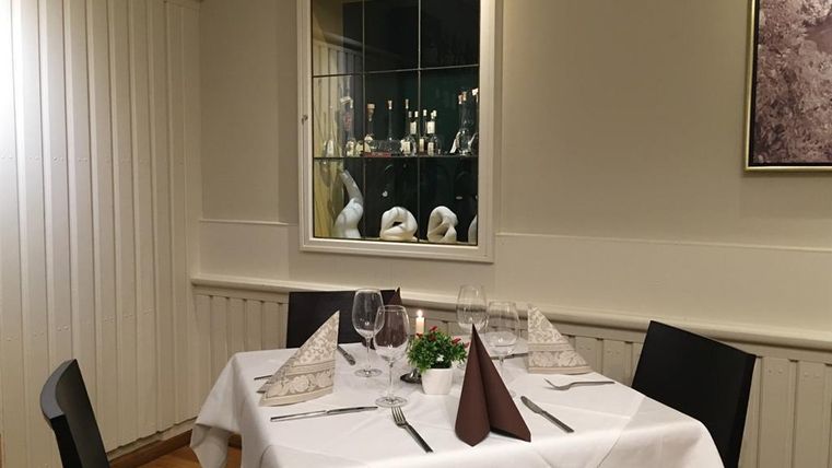 Ein elegant gedeckter Tisch in einem Restaurant mit weißen Tischdecken und Faltservietten. Im Hintergrund sind Vitrinen mit Dekorationsgegenständen zu sehen.