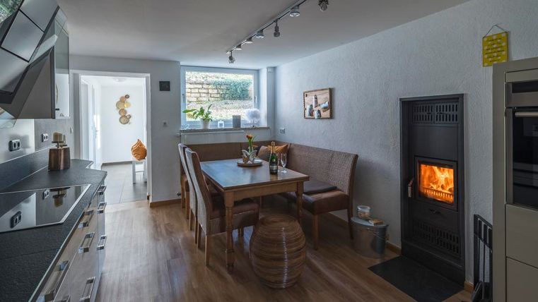 Eine moderne Küche mit einem gemütlichen Tisch und einem Kamin. Der Raum ist hell und einladend, mit Holzfußboden und Fenstern, die Tageslicht hereinströmen.