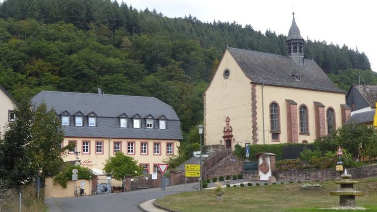 Kirche und Gebäude in Auw am Pilgerweg Speicher mit bewaldetem Hügel im Hintergrund.
