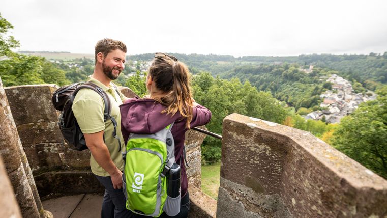 Un couple se tient sur un point de vue et profite de la vue sur la vallée verte. Ils portent des sacs à dos et semblent heureux et détendus.