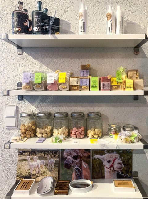 Ein Regal mit verschiedenen Produkten, darunter Gläser mit bunten Leckereien und Kräutern. Auf der unteren Ebene sind auch Fotos von Tieren und kleine Utensilien zu sehen.