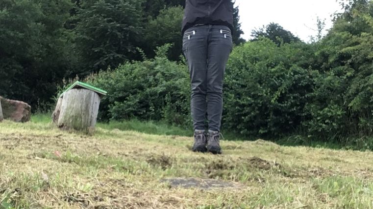 Person steht auf einer Wiese mit erhobenen Armen, umgeben von Bäumen.