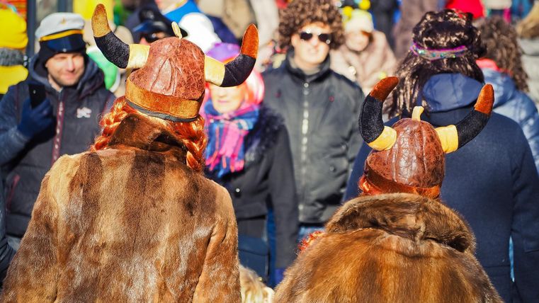 Zwei Personen in Vikinverkleidung mit Hörnerhelmen stehen inmitten einer bunten Menge. Es herrscht eine festliche Stimmung bei einer Veranstaltung oder Parade.