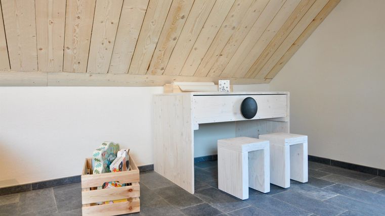 A modern room with a simple table and two stools. In one corner, there is a box with decorative elements.