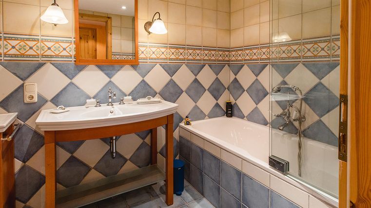 Ein modernes Badezimmer mit einer Badewanne und einem Waschbecken. Die Wände sind mit blauen und weißen Fliesen dekoriert.