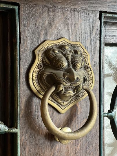 Een kunstzinnige deurklopper in de vorm van een leeuwenkop van brons. Hij is aan een houten deur bevestigd en geeft de entree een elegante uitstraling.
