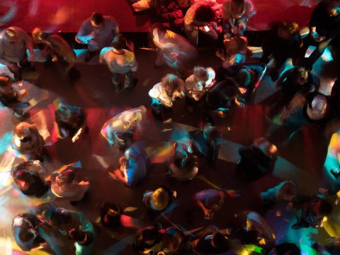 A lively dance floor with many people moving. Colorful lights cast a fascinating glow on the scene.
