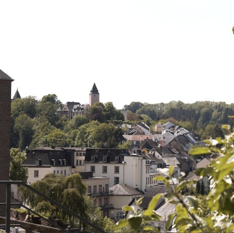 Panoramic view of Kyllburg with a church tower in the foreground, surrounded by houses and green trees under a blue sky., © TI Bitburger Land