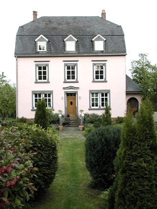 Rosafarbenes Herrenhaus mit grauem Dach, symmetrischen Fenstern und gepflegtem Garten., © Conny Meier