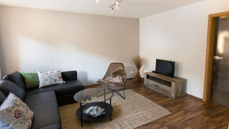 Ein modernes Wohnzimmer mit einem bequemen Sofa und einem rundenGlas-Tisch. Eine dekorative Pflanze und ein Fernseher komplettieren den Raum.