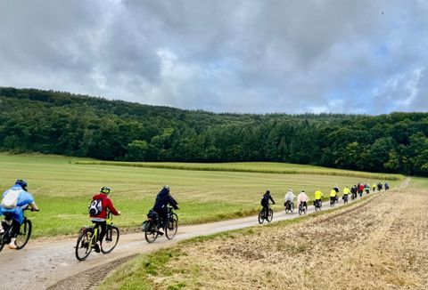 Quatre personnes se tiennent devant un café et posent avec un vélo électrique. Elles sourient et portent des vêtements de sport.