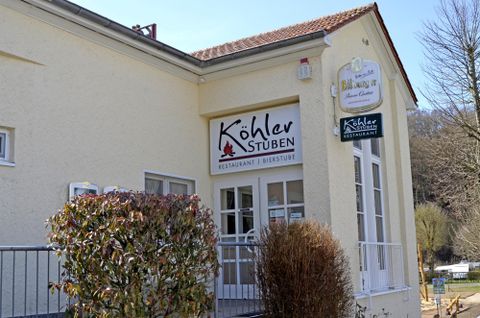 Een restaurant met de naam „Köhler Stuben“ is aan een lichte muur te zien. Voor de ingang staan enkele planten.