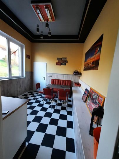 Ein gemütlicher Raum mit schwarz-weißem Schachbrettboden und roten Stühlen. An der Wand hängen verschiedene Dekorationen und Plakate.