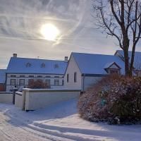Une maison hivernale couverte de neige sous un ciel clair. Le soleil brille et donne à la scène une lumière chaude.