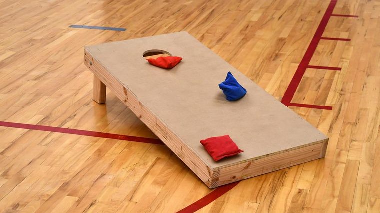 Een houten speelbord voor cornhole met drie kleurrijke vakken. Het bord staat op een met hout beklede ondergrond.