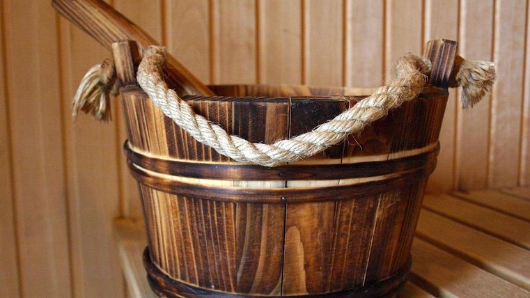 A wooden container with a rope handle is standing in a sauna. The natural wood color blends well with the surroundings.