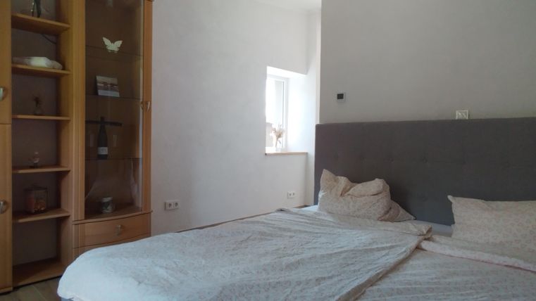 Ein gemütliches Schlafzimmer mit einem großen Bett und einer grauen Kopfteilwand. Auf der linken Seite befindet sich ein rollbarer Schrank mit offenen Regalen.