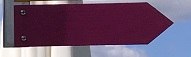 A purple, arrow-shaped sign is attached to a wall. The background shows a blue sky with clouds.