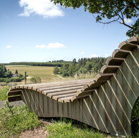 Houten bank met uitzicht op groene velden en bossen onder een blauwe hemel in Neidenbach., © TI Bitburger Land - Monika Mayer