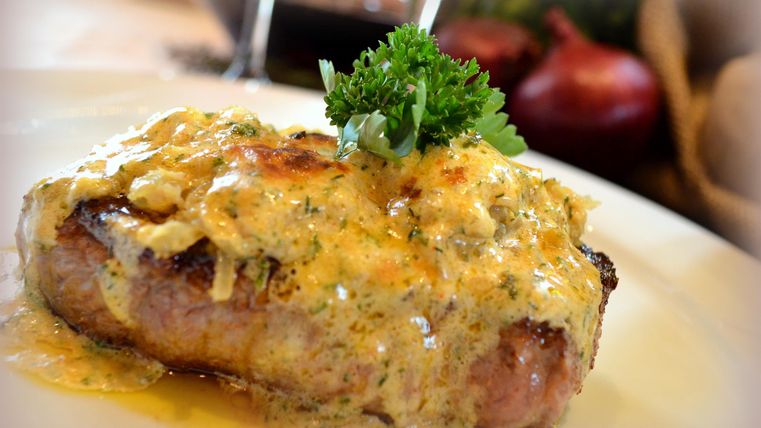 A juicy piece of meat garnished with a creamy sauce and fresh parsley. The dish looks delicious and is perfect for enjoyment.