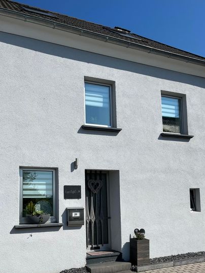 Ein modernes, weißes Haus mit großen Fenstern und einer stilvollen Eingangstür. Der Himmel ist klar und blau.