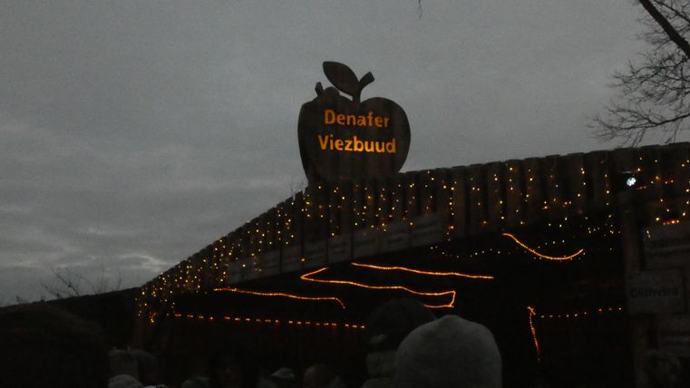 Ein festlich dekorierter Eingang zu einem Veranstaltungsgelände mit einer großen Apfelgrafik. Die Beleuchtung sorgt für eine angenehme Atmosphäre in der Dämmerung.