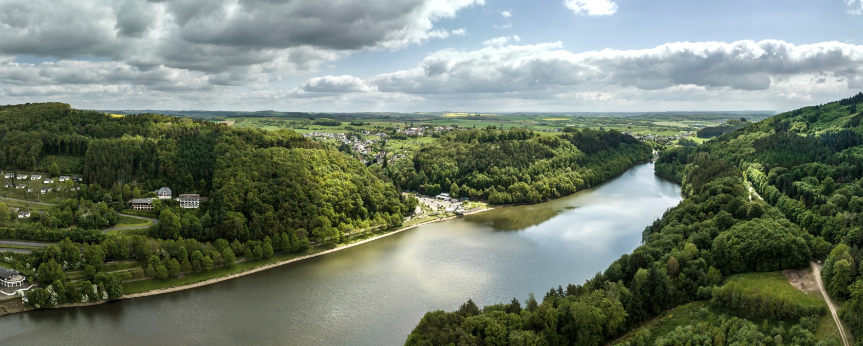 Aerial view of the Bitburg reservoir in Biersdorf am See, surrounded by green forests and hills. The sky is partly cloudy and partly sunny., © Eifel-Tourismus GmbH, Dominik Ketz