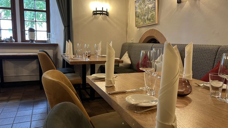 Ein gemütliches Restaurant mit schön eingedeckten Tischen. Die Wände sind hell und es gibt großzügige Fenster, die Tageslicht hereinlassen.