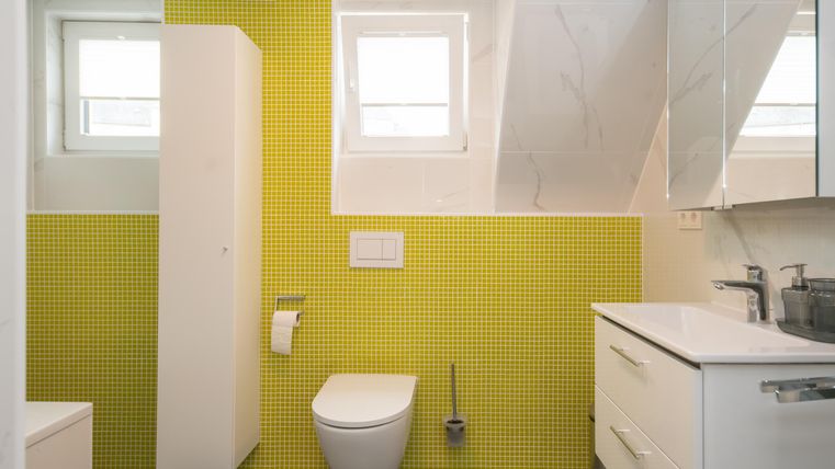 Een moderne badkamer met gele tegels en witte meubels. Er is een raam en een douche.