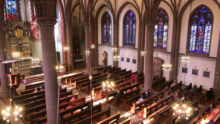 A beautiful church with high ceilings and colorful windows. The benches are neatly arranged and the light falls gently through the windows.