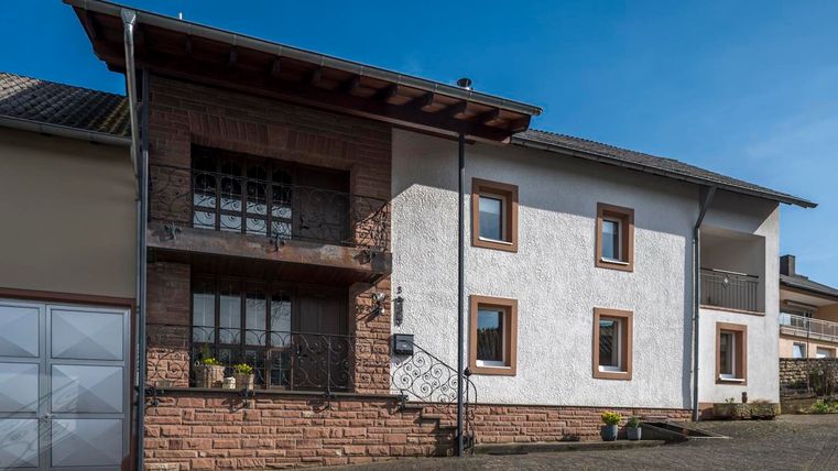 Ein modernes Wohnhaus mit einer Kombination aus weißem Putz und Steinmauer. Die Fassade hat große Fenster und einen einladenden Eingangsbereich.