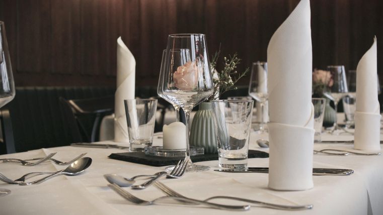 Ein elegant eingerichteter Tisch mit gedeckten Gläsern und gefalteten Servietten. Ein kleines Blumengesteck und Kerzen sorgen für eine gemütliche Atmosphäre.