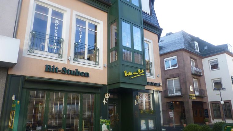Ein Restaurant mit einem modernen, grünen Balkon und großen Fenstern. Die Fassade hat eine freundliche, einladende Ausstrahlung.