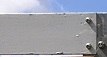 Close-up of a gray sign with screws, in front of a blue sky.