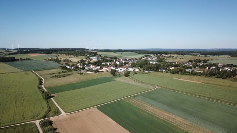 Luchtfoto van Idenheim met velden en windturbines op de achtergrond.