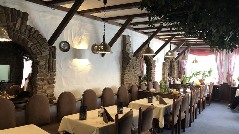 Un restaurant confortable avec une décoration en bois et de longues tables. Les murs sont décorés de briques et de plantes, ce qui crée une ambiance accueillante.