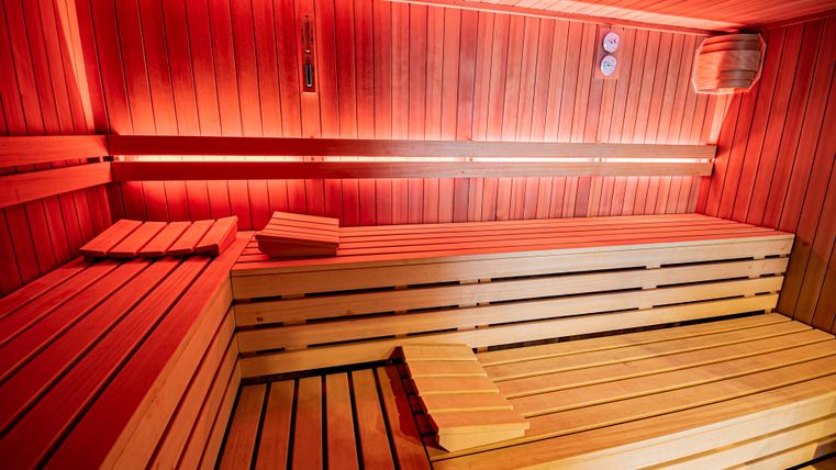 A modern sauna with wooden benches and soft red light. The walls are made of wood, creating a relaxing atmosphere.